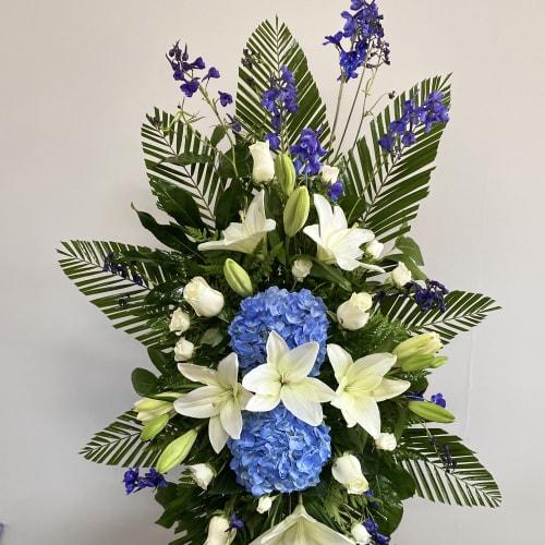 Tall floral standing spray with white lilies, blue hydrangeas, and purple flowers