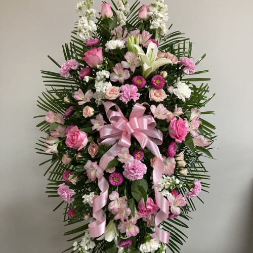 Pink and white funeral spray with roses, lilies, and ribbon