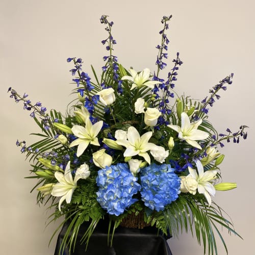 Large floral arrangement with white lilies, blue hydrangeas, and purple flowers