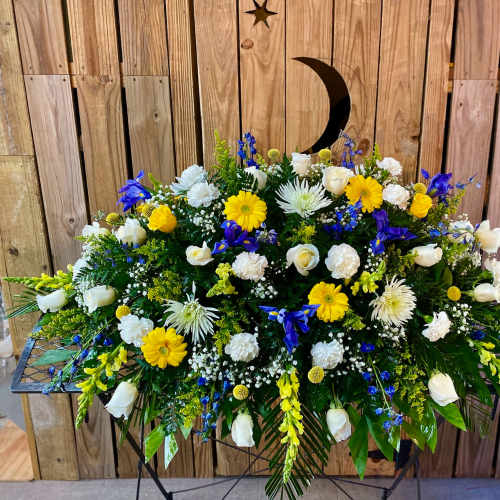 Large funeral spray with white, yellow, and blue flowers on a stand