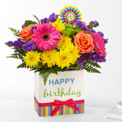 Bright mixed birthday flower arrangement in a white cube vase with Happy Birthday text and ribbon.