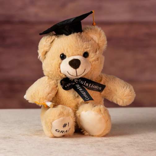 Plush tan teddy bear wearing a black graduation cap and ribbon holding a small diploma