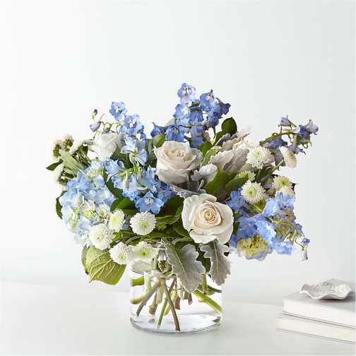 Low bouquet of blue delphinium and white roses in a clear glass vase