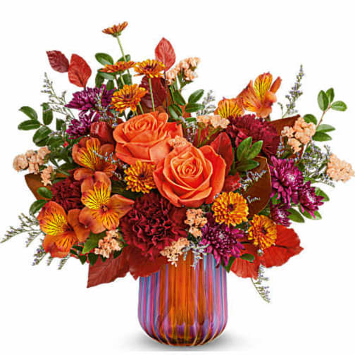 Orange roses and mixed fall flowers in a striped glass vase