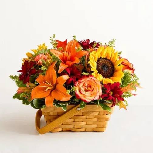 Basket of orange lilies, yellow sunflower, red blooms, and roses in a woven basket.