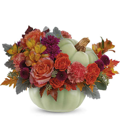 Low autumn bouquet of orange and burgundy flowers in a light green ceramic pumpkin container