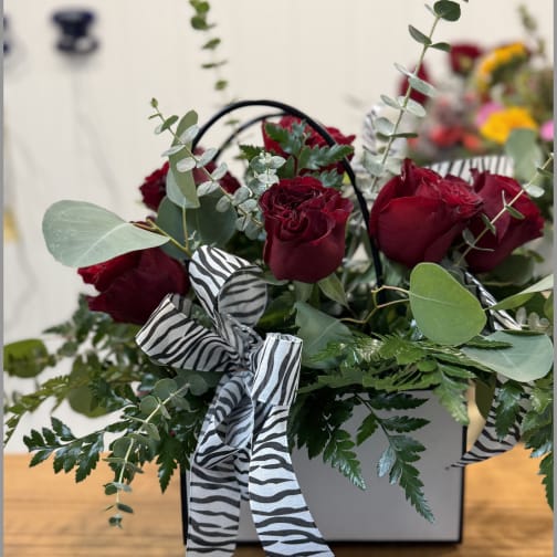 Red roses in a white box with zebra-print ribbon and greenery