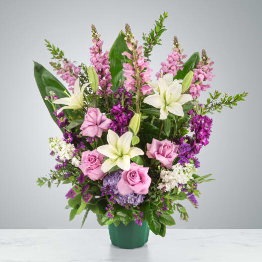 Tall pink and purple arrangement with white lilies and roses in a green container