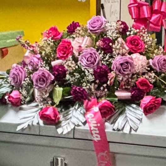 Pink and lavender rose arrangement on a casket with ribbon accents