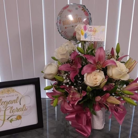 Pink lilies and white roses in a vase with a birthday balloon