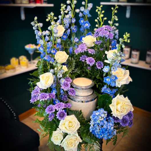 Tall floral arrangement with white roses, blue delphinium, and purple mums around a candle