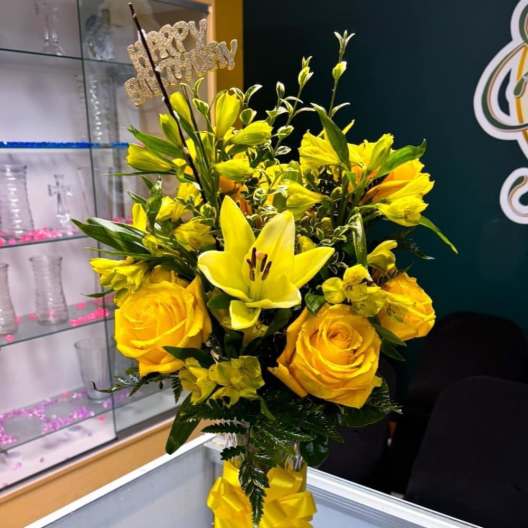 Yellow roses and lilies in a glass vase with a yellow ribbon