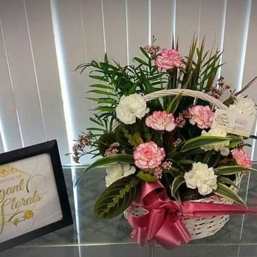Pink and white carnations in a white basket with a pink ribbon