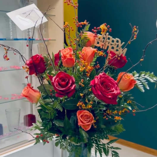 Mixed rose arrangement in a glass vase with a birthday sign