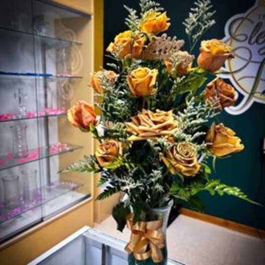 Tall bouquet of orange roses in a gold vase with a ribbon