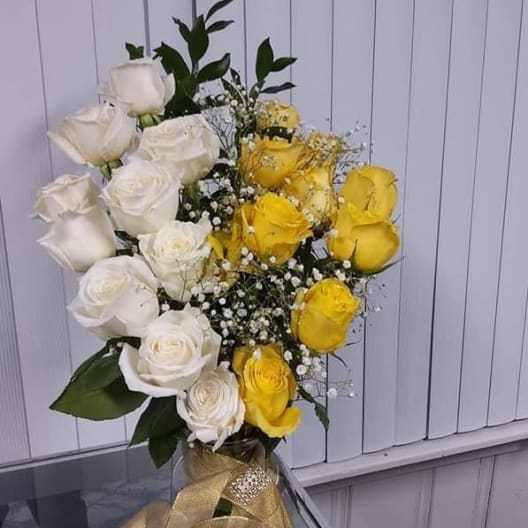 Bouquet of white and yellow roses in a clear vase with a gold ribbon