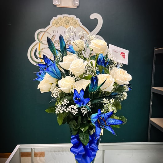 White roses and blue lilies in a glass vase with a blue ribbon