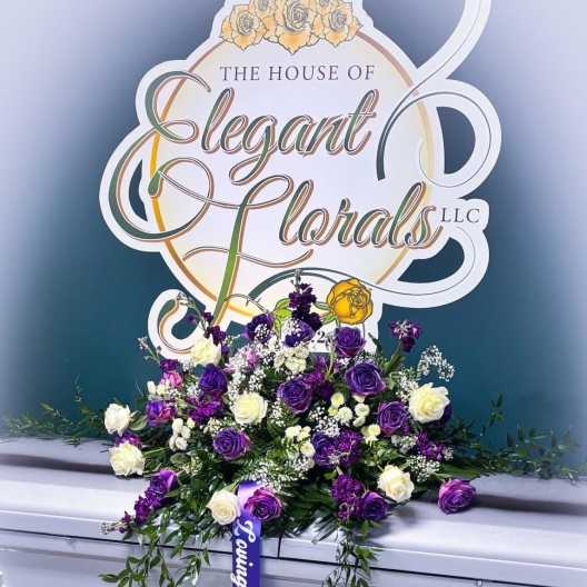 Purple and white rose arrangement on a silver casket with a ribbon