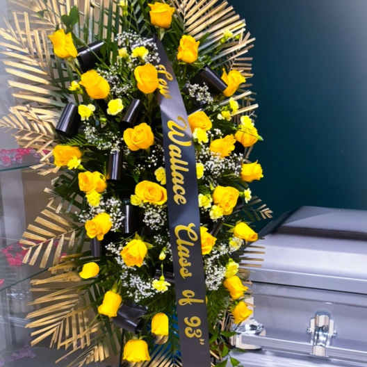 Standing floral spray of yellow roses with a black ribbon on an easel
