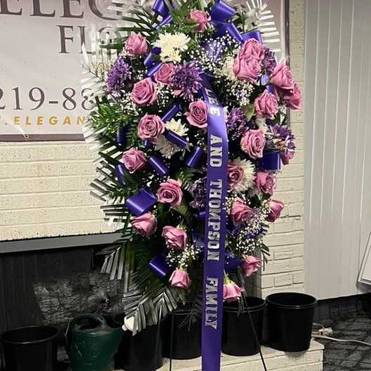 Standing sympathy spray with pink roses and purple flowers on an easel