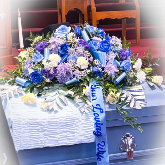 Blue and white floral casket spray with ribbon on a coffin
