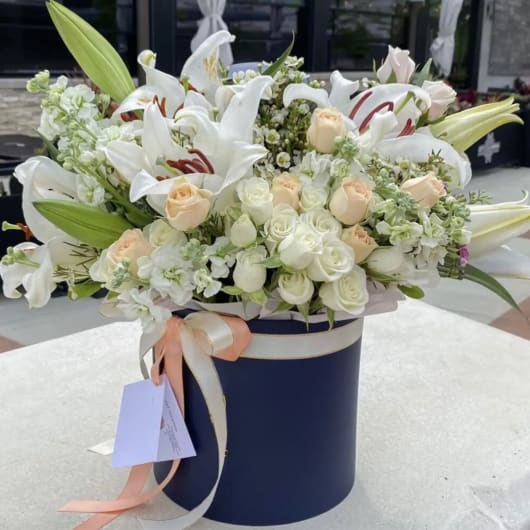 White lilies and pale roses arranged in a navy hatbox