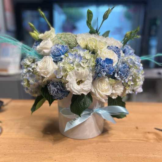 Blue and white flower arrangement in a round box with ribbon