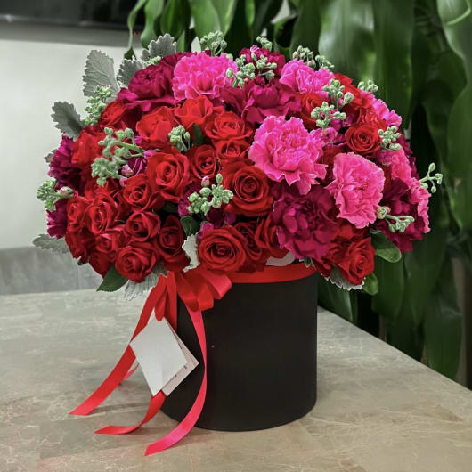 Red and pink rose bouquet in a black hat box with ribbon