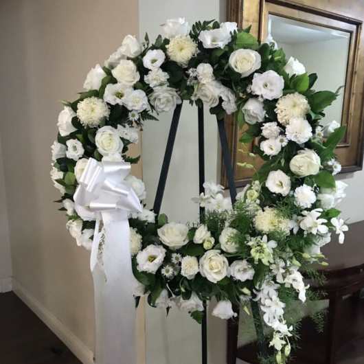 White floral wreath on a black stand with a white ribbon