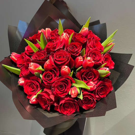 Bouquet of red roses and pink tulips wrapped in black paper