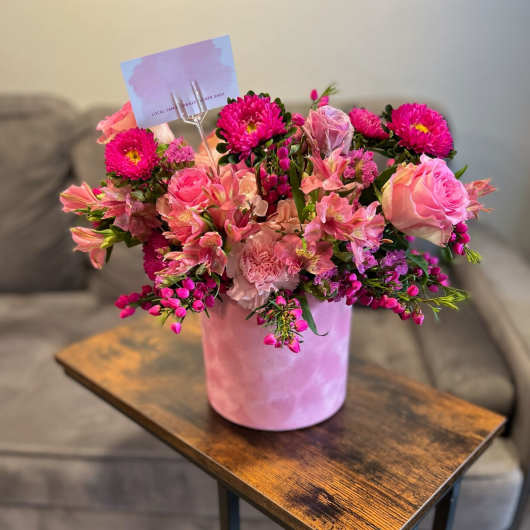 Pink mixed flower arrangement in a pink vase on a wooden table