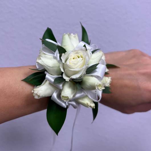 White rose wrist corsage with ribbon and dark green leaves