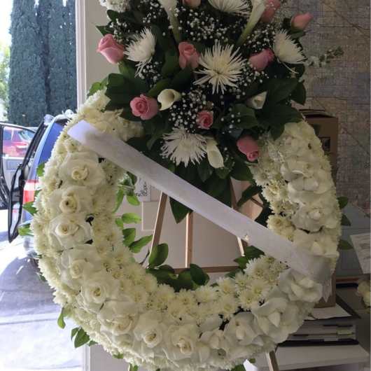 Large white floral wreath with pink roses and a ribbon sash