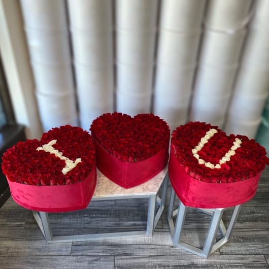 Three heart-shaped rose arrangements in red boxes on stands