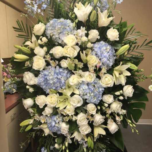 Large white and pale blue floral spray with roses, lilies, and hydrangeas