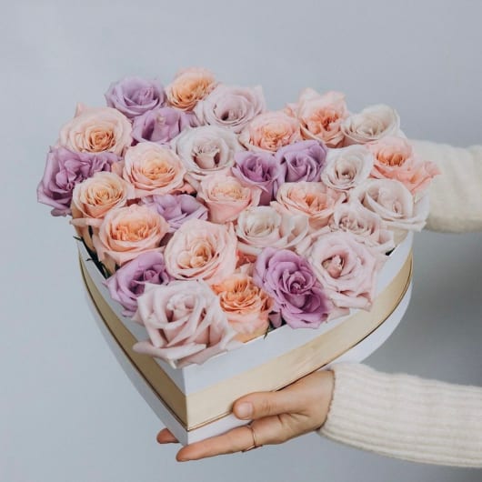 Heart-shaped box of pastel roses held in two hands