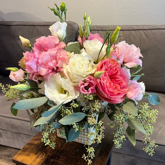 Pink and white bouquet in a square vase with trailing greenery