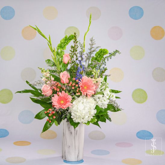 Pink gerberas and roses in a white vase with white hydrangea and tall greenery