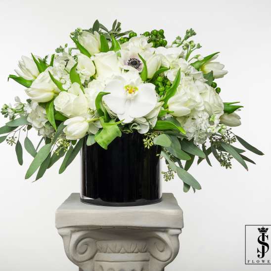 White floral arrangement in a black vase with trailing greenery