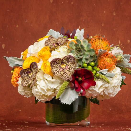 Mixed bouquet in a glass vase with white hydrangeas, yellow roses, and orange accents