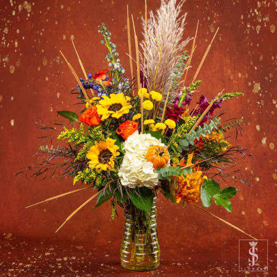 Mixed bouquet in a clear glass vase with sunflowers, roses, and white hydrangea