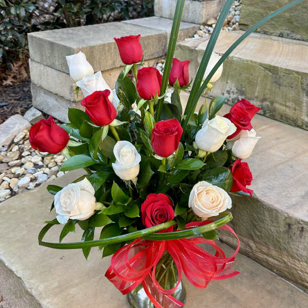 Red and white roses in a glass vase with a red ribbon