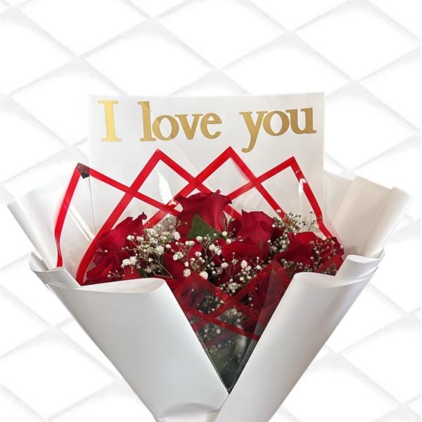 Red roses wrapped in white paper with a gold "I love you" card