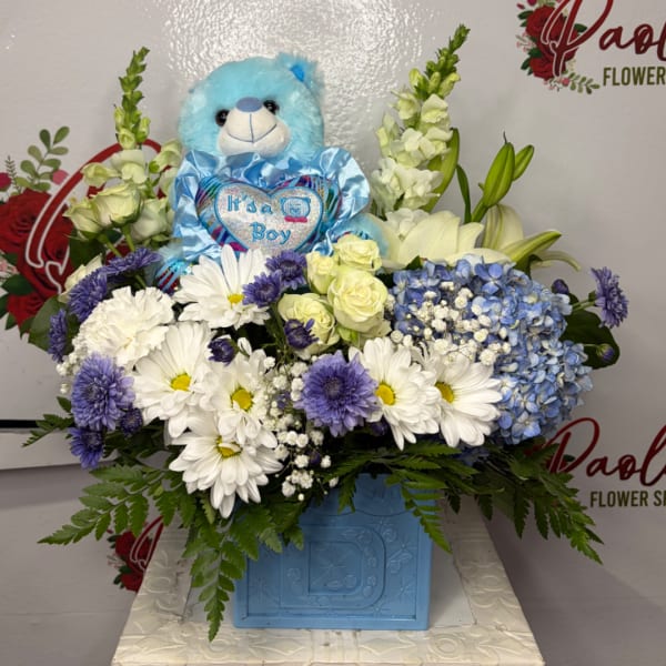 Blue teddy bear in a flower arrangement with white and purple blooms