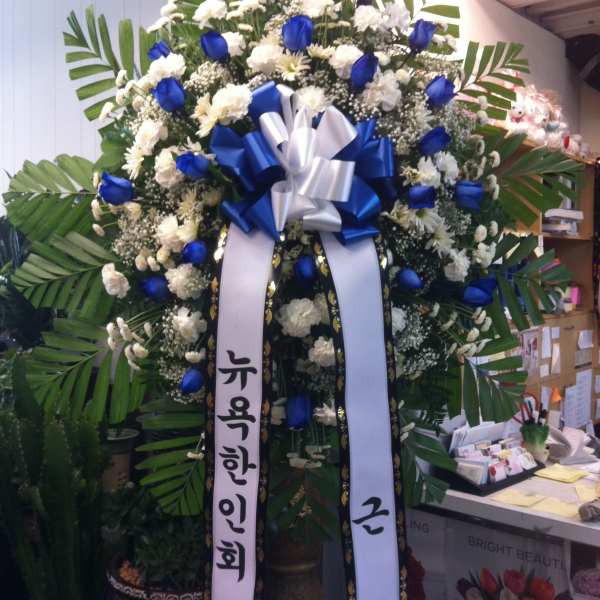 Large standing floral wreath with blue and white flowers and ribbon