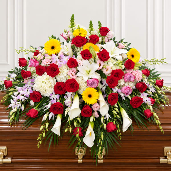 Large floral spray on a casket with red roses, white lilies, and yellow daisies