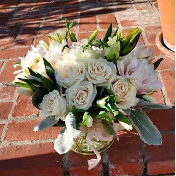 Low glass vase of white roses and pale blooms arranged in a rounded cluster