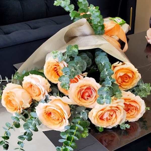 Bouquet of peach roses with eucalyptus in beige wrap resting on a black table