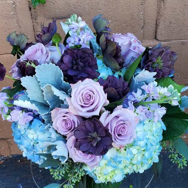 Lavender roses and deep purple blooms arranged with blue hydrangeas in a rounded bouquet