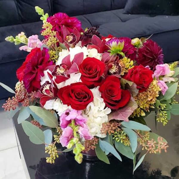 Low arrangement of red roses, orchids, and white hydrangeas in a black vase on a coffee table